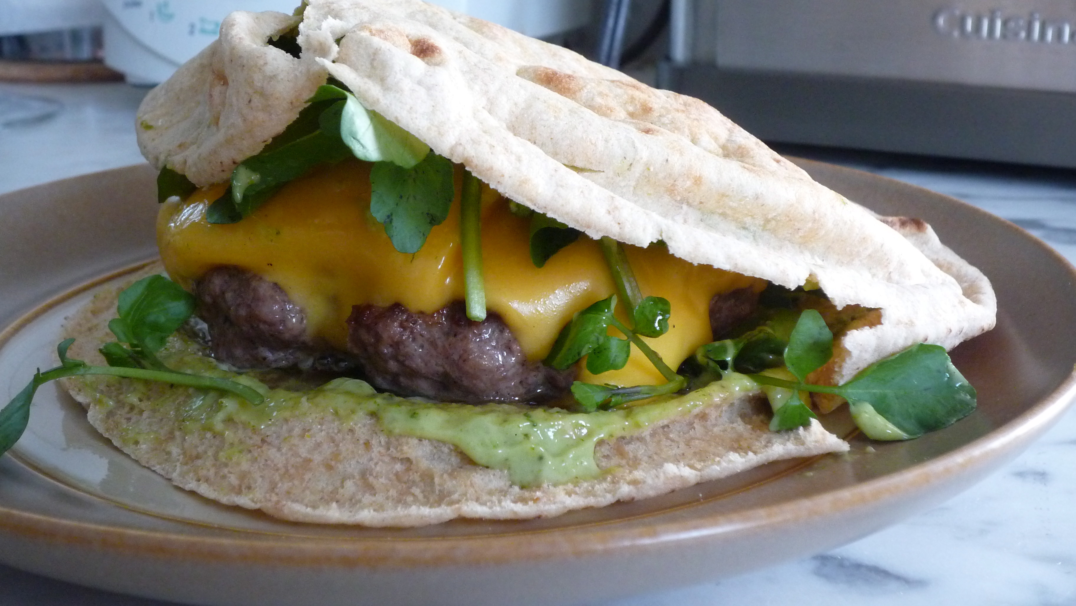 Cheeseburger with arugula topped with pesto mayonnaise in a low carb pita